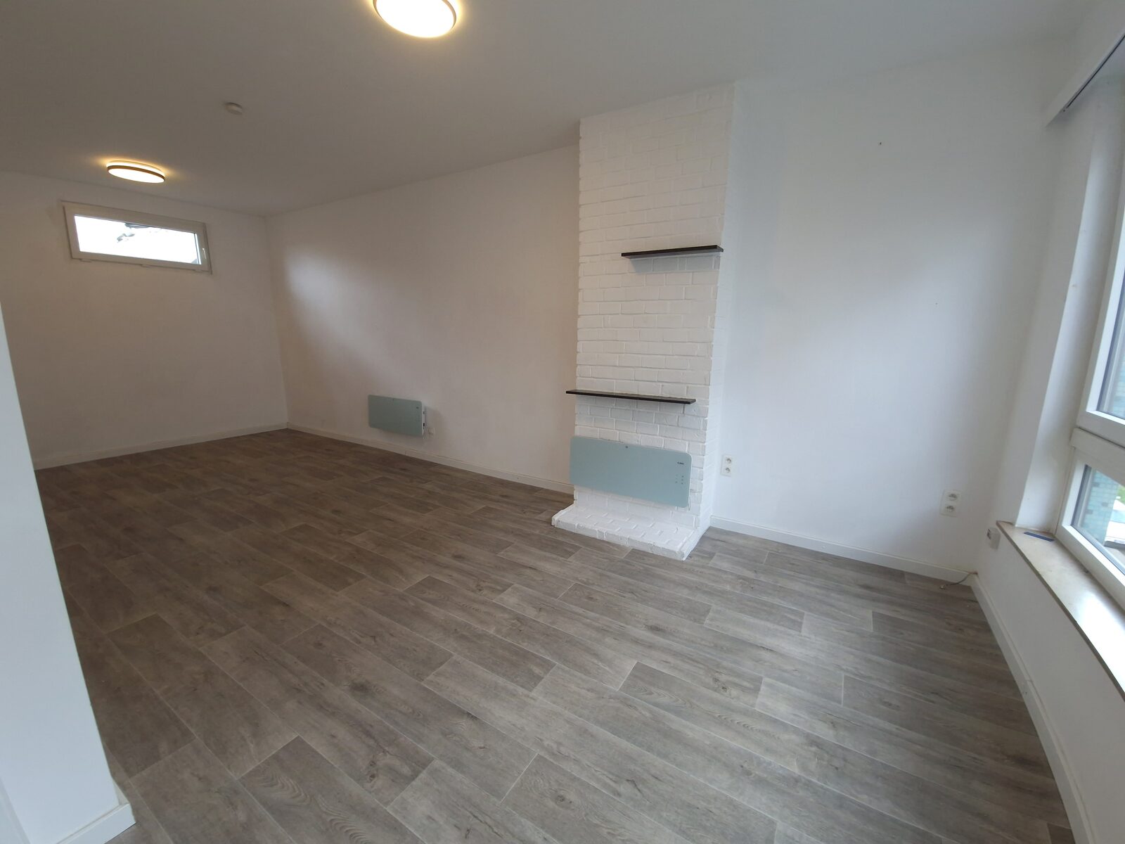 Wit geschilderde bakstenen schouwwand met wandplanken in de leefruimte van de studio